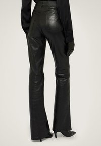 Černé kožené kalhoty s rozšířenými nohavicemi, hladkou texturou, vysokým pasem a zadními kapsami, v kombinaci s těsnými černými rukavicemi a botami na vysokém podpatku.