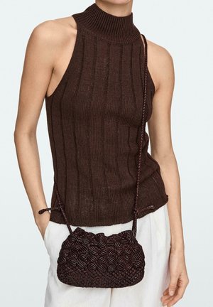 Ärmelloses dunkelbraunes, gerippt gestricktes Top kombiniert mit weißen Hosen und einer strukturierten dunkelbraunen kleinen Schultertasche.