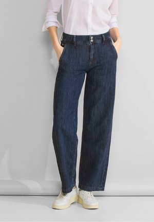 Jeans a vita alta e gamba larga in denim indaco scuro, con chiusura a bottone e tasche laterali, abbinati a sneakers bianche.