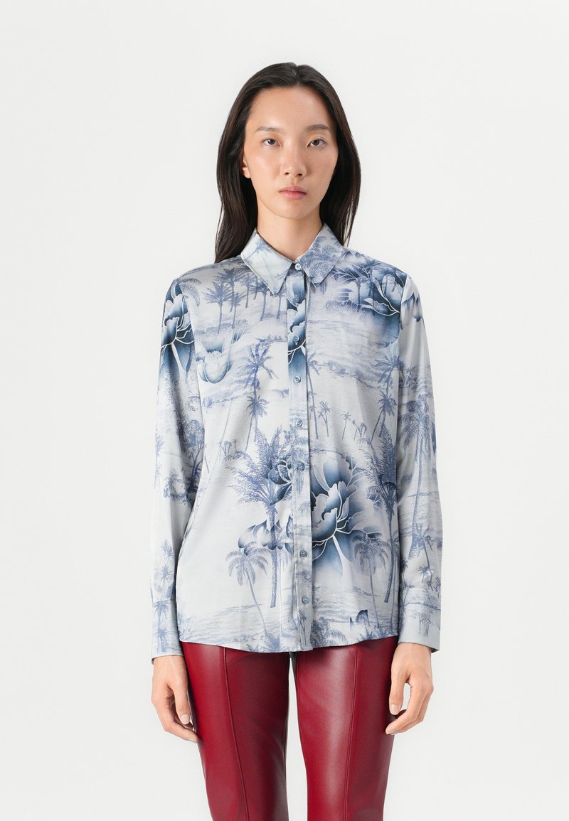 Camicia a bottoni in tessuto setoso, con una base azzurra chiara e motivi di palme e fiori in blu scuro. Maniche lunghe e design del collo classico.