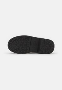 Suela de zapato de goma negra con un diseño de huella texturizada, que presenta tacos profundos y un borde suave para mejorar la tracción y la durabilidad.