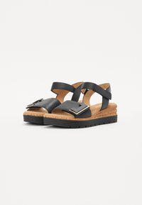 Black sandals with two cross straps; features a wide front strap with a metallic accent. Cork footbed and black rubber sole for support.