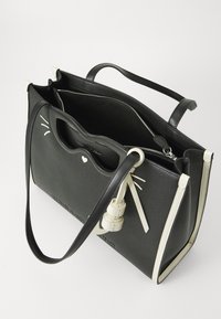 Crna kožna torba za rame s bijelim detaljima, gornjim ručkama i zabavnim dizajnom s brkovima i detaljem srca. Zatvaranje na zip, prostrano unutrašnjost.