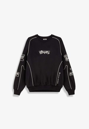 Sudadera negra con acentos y costuras blancas, que presenta varios logotipos y texto en las mangas, cuello redondo y puños acanalados.
