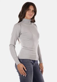Maglione grigio a collo alto realizzato in materiale morbido, con maniche lunghe, polsini e orlo a costine e una silhouette aderente. Abbinato a jeans scuri.
