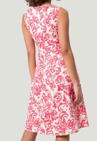 Blumenkleid mit tailliertem Oberteil und schwingendem Rock, mit rosa und korallenfarbenen Mustern auf weißem Hintergrund. Ärmelloses Design, glatte Textur.