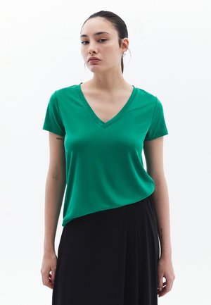 T-shirt vert à manches courtes en V en tissu lisse, avec un design ajusté et un ourlet asymétrique, associé à une jupe noire.