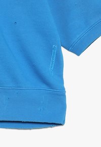 Sudadera in cotone azzurro con orlo e polsini a costine, dotata di un piccolo logo impresso di lato. Texture leggermente consumata.