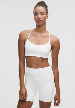 Hvid atletisk crop top med tynde stropper, parret med højtaljede hvide shorts. Glat tekstur, enkelt design, ingen synlige mønstre eller hardware.