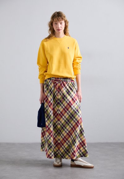 Sudadera amarilla con cuello redondo y puños de canalé, combinada con una falda larga de cuadros de múltiples colores y cintura con cordón. Zapatillas blancas.