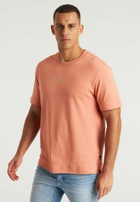 Trumpas rankovės, apvali apykaklė t-shirt šviesiai koralinės spalvos, pagaminta iš minkštos medvilnės. Su subtiliu logotipo grafiku krūtinėje ir įprastu siluetu.