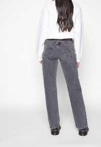 Grå denimjeans med rak passform, synlig sömnad och två bakfickor. Bärs med en vit oversized sweatshirt och svarta skor.