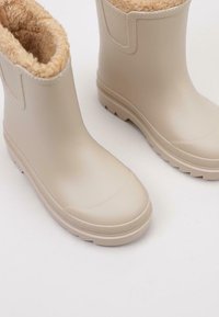 Beige voděodolné gumové boty s měkkou béžovou kožešinou, texturovanou podrážkou a zaoblenou špičkou, s bočními panely pro snadné obouvání.