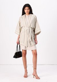Svetlo béžový kimono štýlový kabát s horizontálnymi pruhmi a čiernymi akcentami, sťahovaný v páse zladeným opaskom, spárovaný s neutrálnou sukňou.