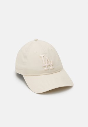 Casquette de baseball beige avec logo "LA" en relief à l'avant, comprenant des œillets cousus et une visière incurvée sur un fond blanc uni.