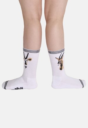 Calcetines blancos de algodón con diseño de jirafa en negro y beige, con puños acanalados rayados en negro y secciones sólidas en el talón y los dedos.
