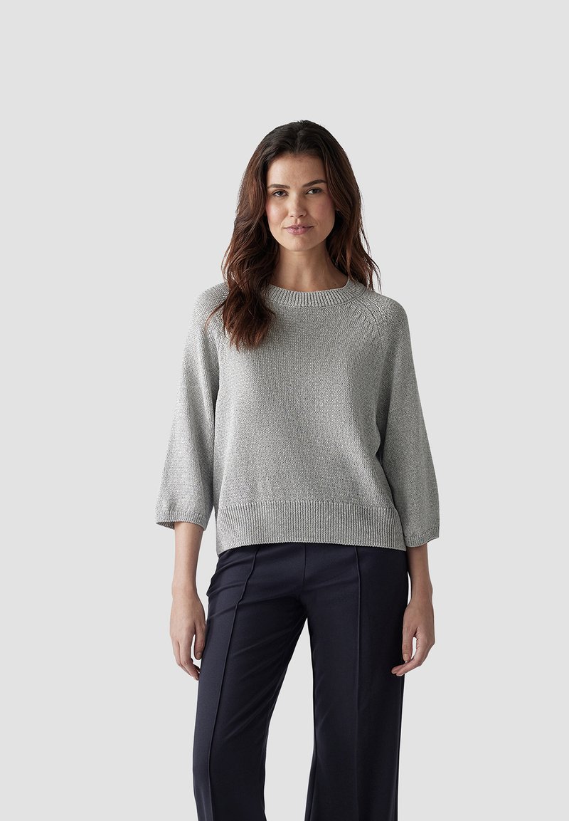 Grauer Strickpullover mit Rundhalsausschnitt, Dreiviertelärmeln und geripptem Saum, kombiniert mit taillierten navyblauen Hosen, vor einem neutralen Hintergrund.