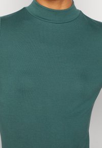 Turkusowy, długi rękaw, golf wykonany z gładkiego materiału, z dopasowanym krojem i prążkowanym, wysokim dekoltem.