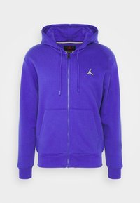 Lila zip-up hoodie i mjukt material. Har en framficka, justerbar dragsko i huva och en liten logotyp på bröstet.