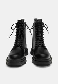 Fekete fűzős bokacsizma sima bőrből, vastag talppal, kerek orral és megerősített fűzőlyukakkal.