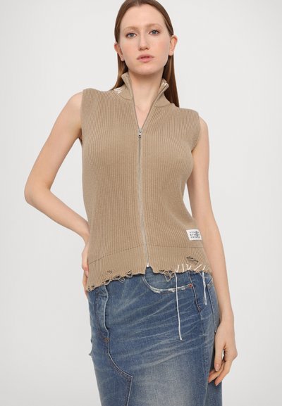 Beige sleeveless knit top with a high collar, front zipper, and frayed hem details, paired with a blue denim skirt.