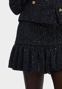 Granatowy zestaw żakietu i spódnicy z tweedu o teksturowanym wykończeniu, z guzikami w kolorze złota i falbaną u dołu spódnicy.