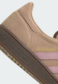 Suède sneakers in lichtbruin met roze strepen. Heeft een textuur van een bruine loopzool en gegraveerd logo in goud aan de zijkant.