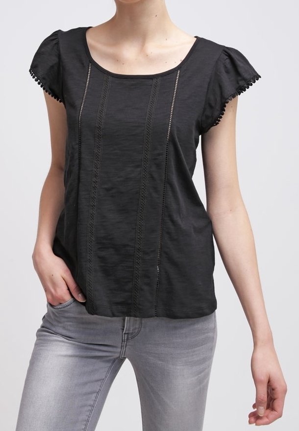 Czarna krótka bluzka z teksturowanej tkaniny, z poziomymi przeszyciami i falbaniastymi brzegami rękawów. Połączona z jasnoszarymi dżinsami.