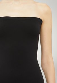 Body nero senza spalline, realizzato in un tessuto liscio e elastico. Caratterizzato da un design aderente, bordo superiore senza cuciture e linee semplici e pulite.