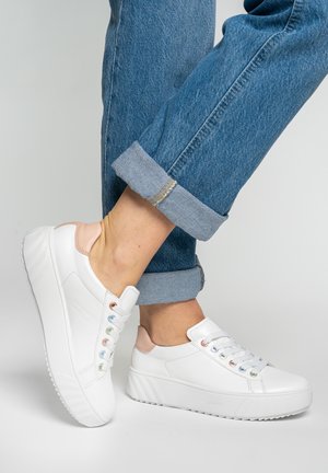 Piedi che indossano sneakers bianche con piattaforma e occhielli color pastello, abbinate a jeans blu risvoltati.