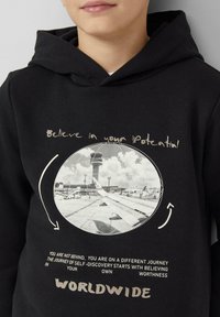 Felpa nera con foto di una torre di controllo aeroportuale e un'ala di aereo, testo motivazionale "Credi nel tuo potenziale" e "In tutto il mondo" sul davanti.