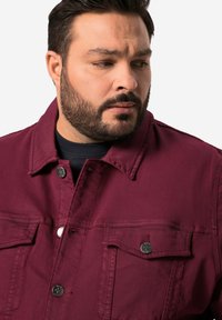 Burgundská džínová bunda s klasickým límcem, dvěma náprsními kapsami a stříbrnými knoflíky. Hladká textura s pevným designem.