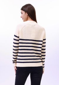 Pull crème avec des rayures navy, présentant une texture côtelée et un col rond, vu de dos avec des manches longues et un ourlet ajusté.