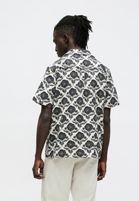 Koszula z krótkim rękawem na białym tle z granatowym kwiatowym wzorem, o luźnym kroju i klasycznym kołnierzyku. Gładka faktura tkaniny.