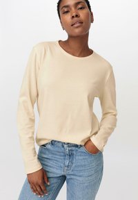 Langärmliges, beiges T-Shirt aus weichem Stoff, mit rundem Ausschnitt und lässiger Passform, kombiniert mit hellblauen Jeans.