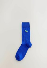 Chaussette bleu vif avec bord-côtes et petite grenouille verte brodée près du haut, présentée sur un fond clair uni.