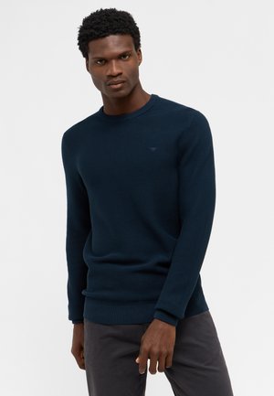 Suéter de punto azul marino con cuello redondo, puños y dobladillo acanalados. Cuenta con un sutil logo en el pecho, fabricado con una suave y texturada tela.