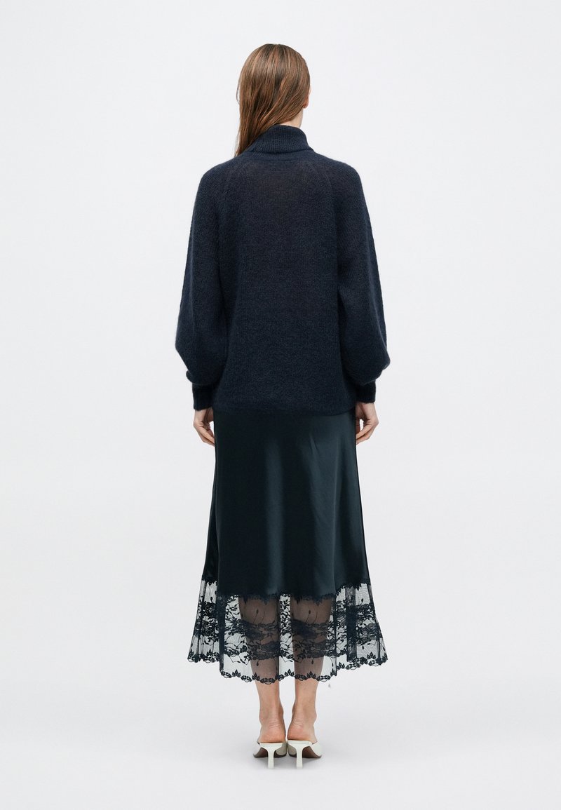 Dark gray oversized sweater with a high neck, paired with a long black satin skirt featuring a lace trim at the hem.