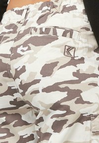 Cargo nohavice v béžovej a hnedej kamuflážnej vzore, s elastickým pásom, bočnými vreckami a vyšívaným logom.