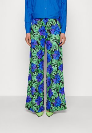 Blumen-mit weitem Bein in Schwarz mit leuchtend blauen Blumen und grünen Blättern. Kombiniert mit einem blauen Hemd und grünen spitzen Absätzen.