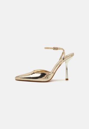 Saltos slingback metálicos dourados com bico pontiagudo, tira fina no tornozelo e superfície refletiva. Apresenta um salto esbelto com um acabamento brilhante.