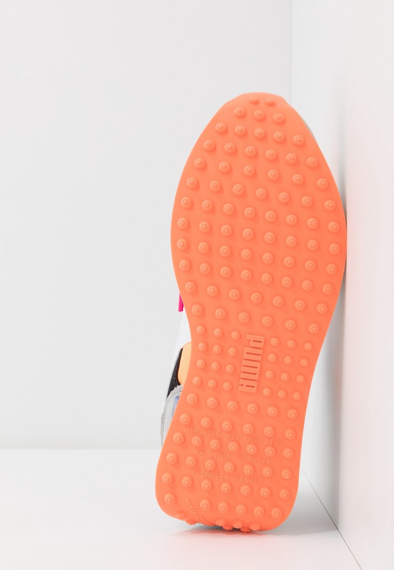 Semelle d'une basket Puma à semelle orange avec des grips circulaires en relief, présentée sur un fond blanc en coin.