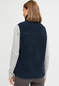 Fleeceställ i marinblått, med hög krage och en texturerad yta. Sammanfogat med en ljusgrå långärmad skjorta under.