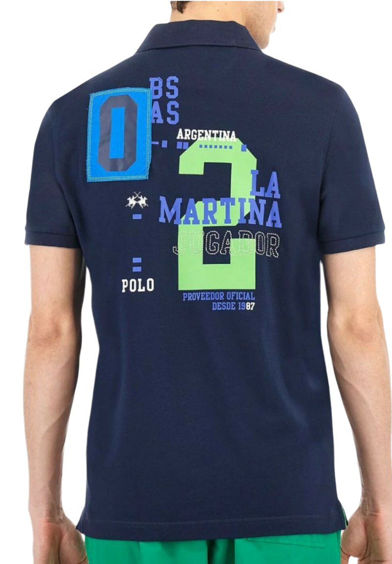 Uomo che indossa una polo blu navy con testo colorato e numero "2" sulla schiena, abbinata a pantaloni corti verdi.