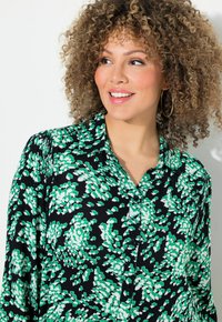 Blusa nera con un motivo floreale verde e bianco, colletto, apertura con bottoni, maniche lunghe e tessuto testurizzato.