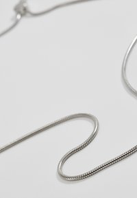 Silver metal snake chain necklace, featuring a smooth, flexible design with a polished finish, laid out on a light background.