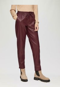 Bordeaux nepleren joggers met een elastische tailleband en zijzakken, gecombineerd met beige enkellaarsjes met zwarte elastische panelen.