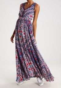 Maxime dress, jossa on sinisen, punaisen ja valkoisen värin kukka- ja geometrinen kuvio; olkaimeton muotoilu, V-pääntie ja valuvat kankaat.
