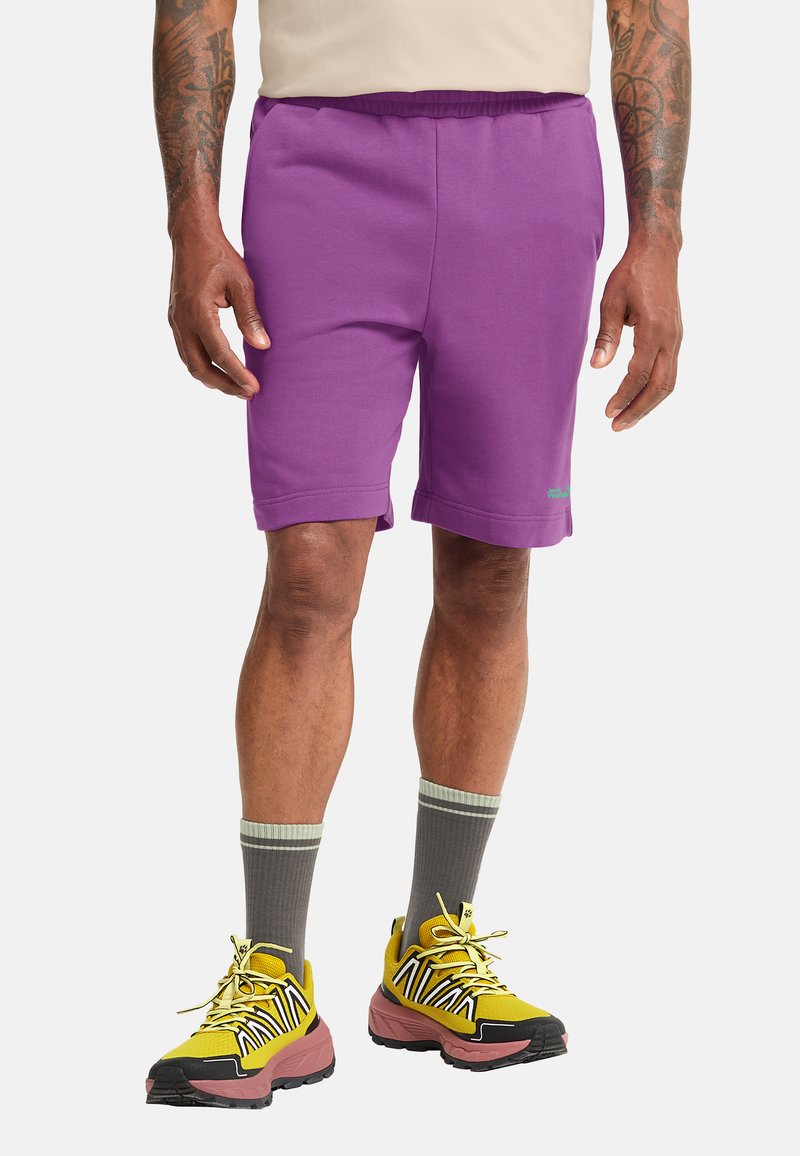 Shorts de sport violets avec une taille élastique, assortis à des baskets jaunes ornées de motifs en zigzag noir et blanc, accompagnés de chaussettes grises.