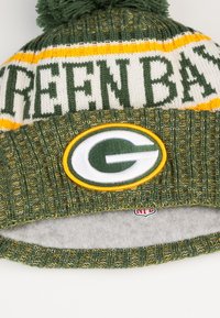 Chapeau en tricot vert avec le texte jaune et blanc "GREENBAY", comportant un patch logo circulaire. Doublure douce, pompon sur le dessus, design texturé avec côtes.